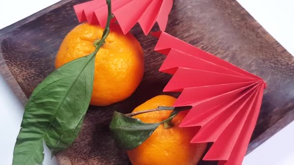 Rotazione di un piatto di legno scuro con ventilatori di carta origami rosso e mandarini. Capodanno cinese vacanza sfondo, creatività, vista dall'alto, 4K video - Filmati, video