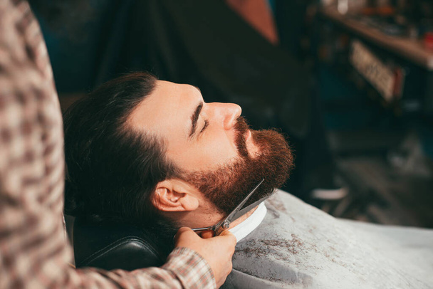 Selective focus of barber making beard haircut with scissors - Фото, изображение