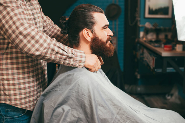 Photo of bearded hipster man sitting in barbershop, making haircut - Foto, Imagem