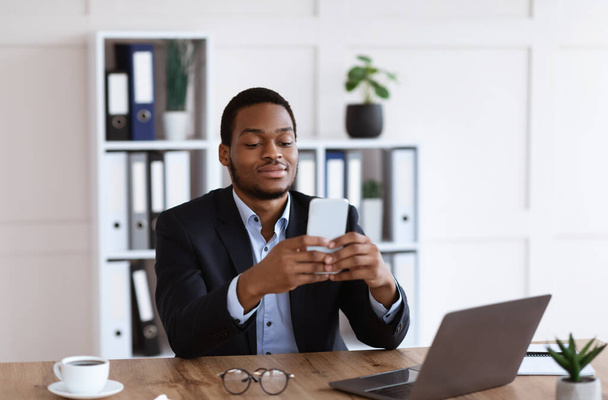 Jonge Afrikaanse man in pak met smartphone op kantoor - Foto, afbeelding