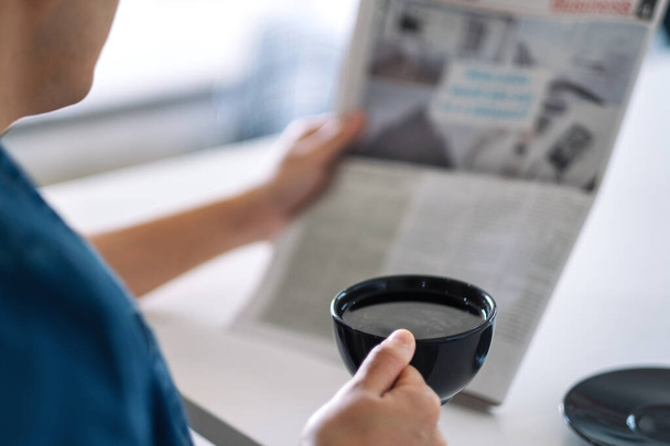 Closeup image of a man reading newspaper and drinking coffee in the morning - Foto, afbeelding