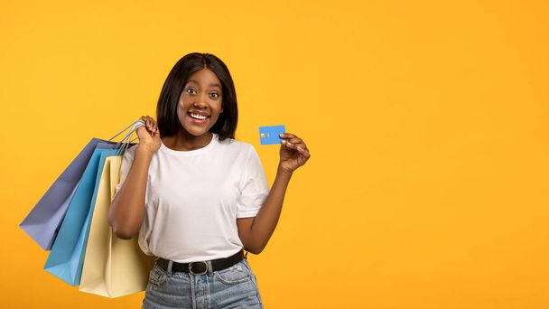 Vrolijke Afrikaans-Amerikaanse vrouw met aankopen tonen credit card - Foto, afbeelding