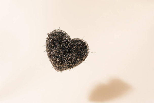 Σφουγγάρι μεταλλικό σε σχήμα καρδιάς - συρματόπλεγμα σε μπεζ φόντο με σκιά σε γωνία 45 μοιρών. - Φωτογραφία, εικόνα