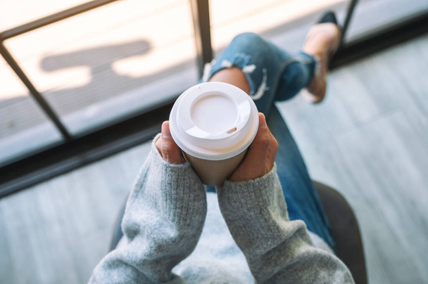 Vista superior de la imagen de una mujer sentada y sosteniendo una taza de papel de café caliente por la mañana - Foto, Imagen