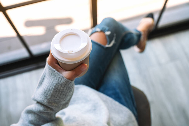 Imagem de vista superior de uma mulher sentada e segurando uma xícara de papel de café quente pela manhã - Foto, Imagem
