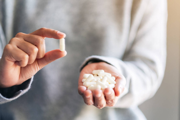 Closeup image of a woman holding and showing white medicine capsules in hand - Foto, afbeelding