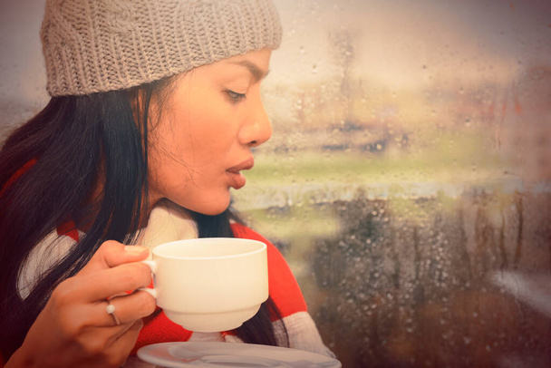 Mitte erwachsene Frau trinkt Kaffee in der Nähe des Fensters an regnerischen und frostigen Tag. Horizontale Form - Foto, Bild