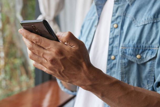 Zoom View vasen käsi nuorten Aasian rento liikemies denim tai farkut paita käyttämällä älypuhelinta kahvilassa. Rento liikemies Tekniikan parissa - Valokuva, kuva