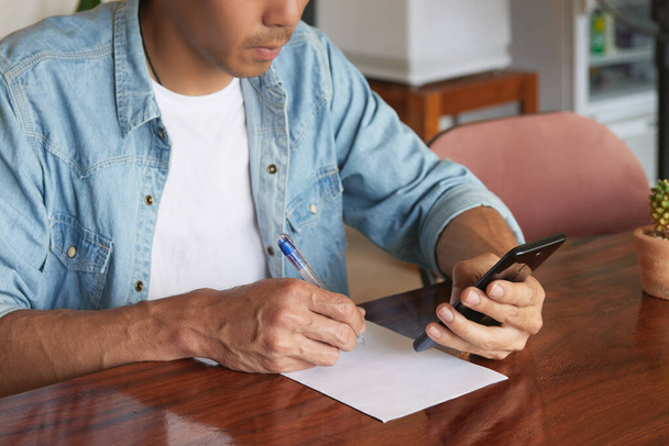 Молодой азиатский бизнесмен в джинсовой рубашке с использованием смартфона и обратите внимание в кофейне. Случайный бизнесмен, работающий с технологиями - Фото, изображение