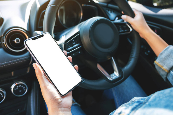 Imagen burlona de una mujer sosteniendo y utilizando el teléfono móvil con pantalla en blanco mientras conduce el coche - Foto, imagen