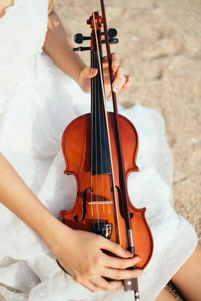 Обрізане зображення скрипки на білому платті жіночі ноги на піщаному пляжі, вертикально
. - Фото, зображення