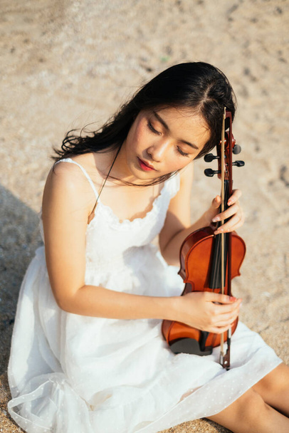 Чорний довге волосся скрипка гравець сидить на піщаному пляжі зі скрипкою на її лагах і закриває очі
. - Фото, зображення