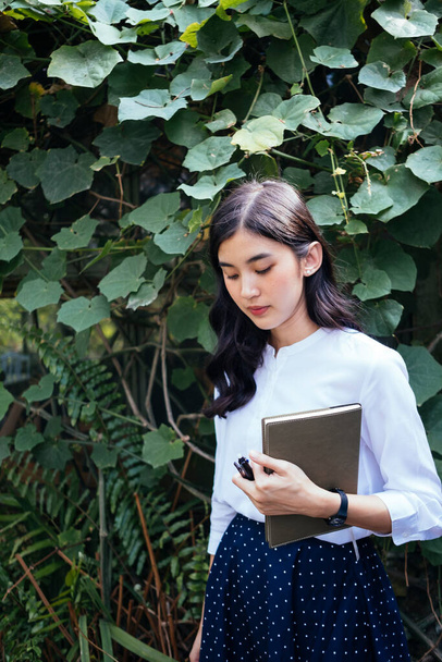 Beautiful asian woman in tropical garden holding a book with her hands, standing at live wall outside stone house. Girl and the book. Novel writer. - Foto, Imagen