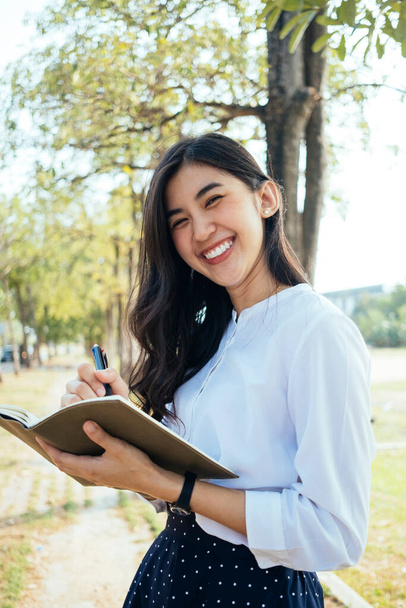 Happy asian woman on white shirt writing a book with happiness feeling, smiling and laughing. Novel writer girl writting with smile. - Foto, imagen