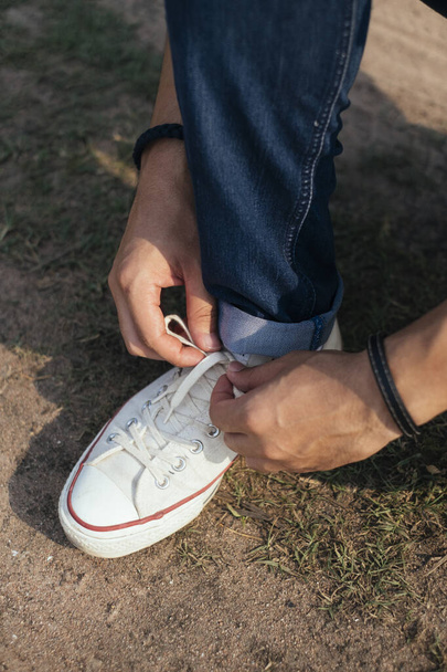 Männlicher Abenteurer sitzt und schnürt seine Schnürsenkel auf dem Schmutzteil. - Foto, Bild