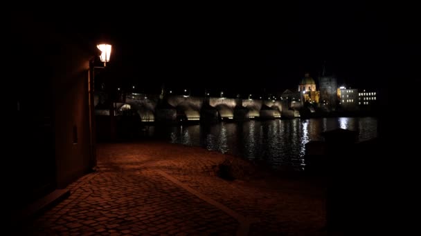 straatverlichting en een verharde stoep voor voetgangers en op zijn beurt een nachtzicht op de Karelsbrug en de verlichting 's nachts en een vloeiende Vltava rivier in het centrum van Praag - Video