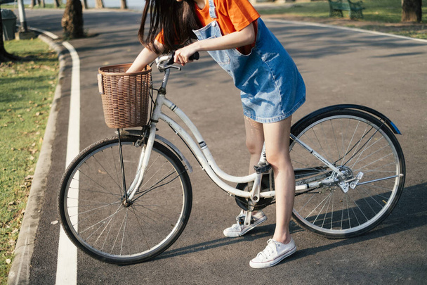 Zugeschnittenes Bild eines weißen Fahrrads zwischen den Beinen einer Frau im Park. - Foto, Bild
