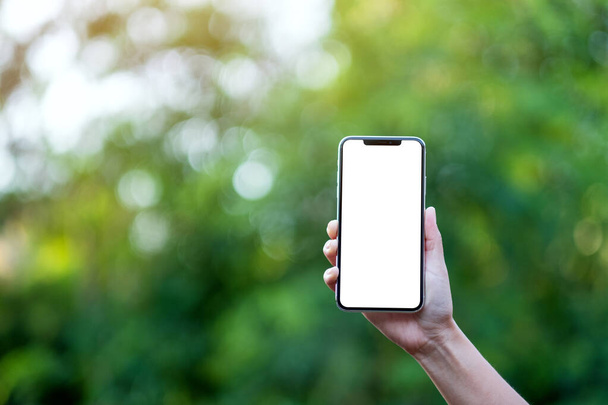 Макет руки, що тримає чорний мобільний телефон з порожнім екраном стільниці з зеленим фоном природи
 - Фото, зображення