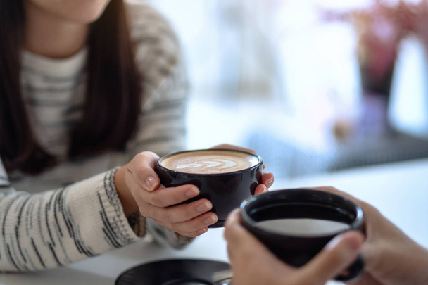 Крупним планом зображення чоловіка і жінки, що тримає дві чашки кави разом
 - Фото, зображення