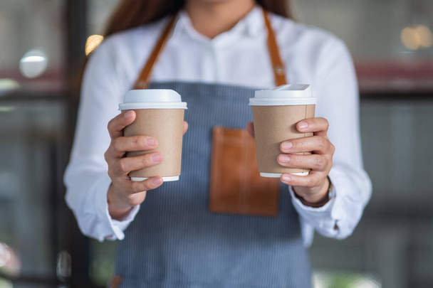 Σερβιτόρα που κρατάει και σερβίρει δύο χάρτινα φλιτζάνια ζεστού καφέ στο καφέ - Φωτογραφία, εικόνα