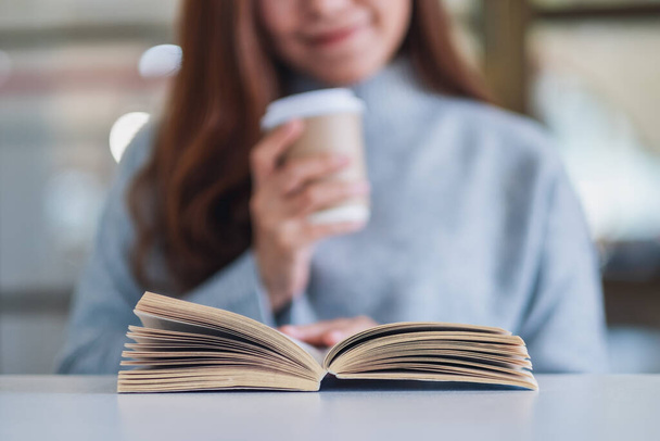 Nahaufnahme einer Frau, die ein Buch liest, während sie Kaffee auf einem Holztisch trinkt - Foto, Bild