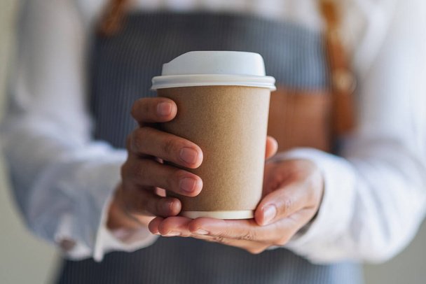 A waitress holding and serving a paper cup of hot coffee in cafe - Photo, Image