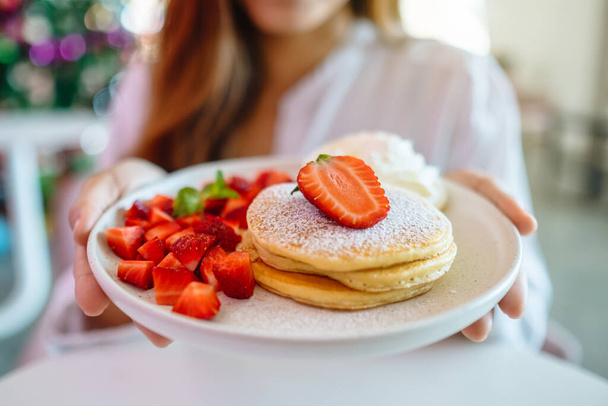 A woman holding and showing a plate of pancakes with strawberries and whipped cream  - Foto, imagen