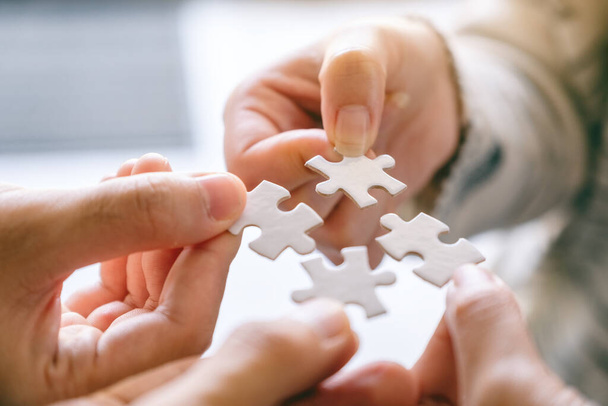 Closeup image of many people holding and putting a piece of white jigsaw puzzle together - 写真・画像
