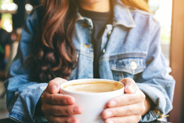 Szoros kép egy nőről, aki egy csésze forró kávét tart az asztalon. - Fotó, kép