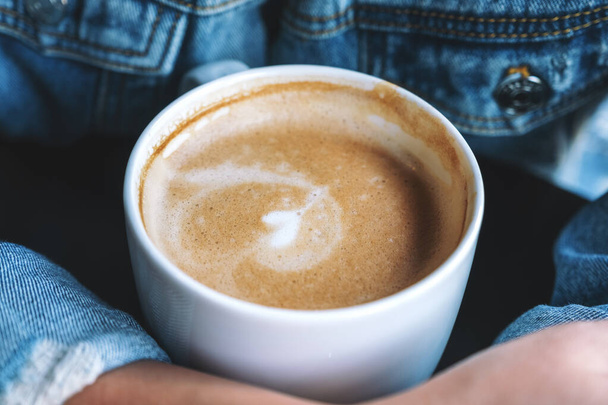 Immagine da primo piano di una donna che tiene una tazza di caffè al latte caldo sul tavolo - Foto, immagini