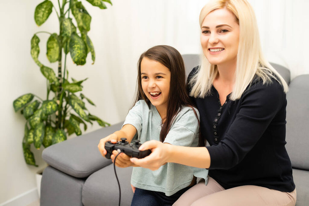 Mother and daughter sittingr in a playroom, playing video games and having fun. - Zdjęcie, obraz