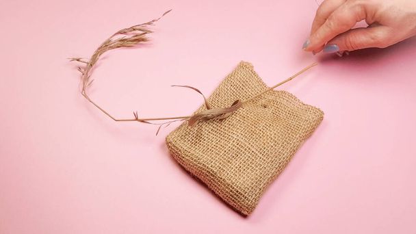 Florista manos preparan hierba seca y bolsa de lona para la composición, sobre fondo rosa, concepto de bricolaje. - Foto, Imagen
