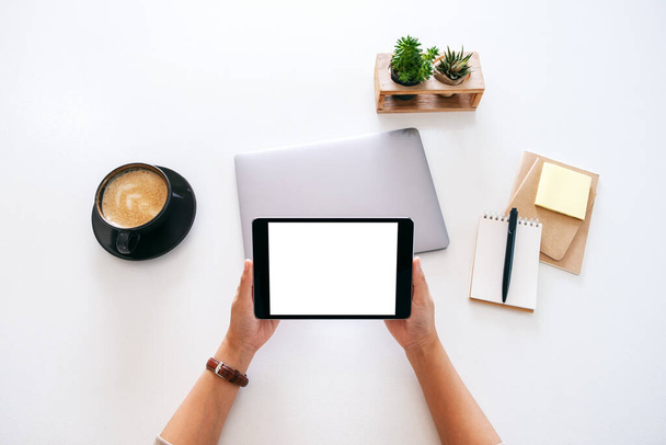 Вид зверху макет зображення рук, що тримають планшет з порожнім білим екраном і ноутбуком на дерев'яному столі в офісі
 - Фото, зображення