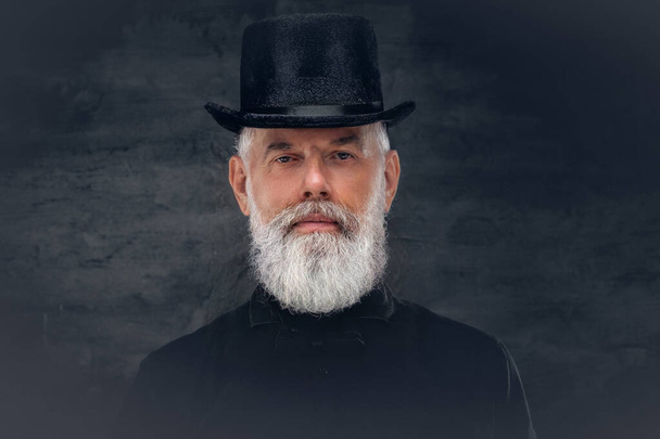 Old man with top hat and in black clothing posing in dark background - Photo, Image