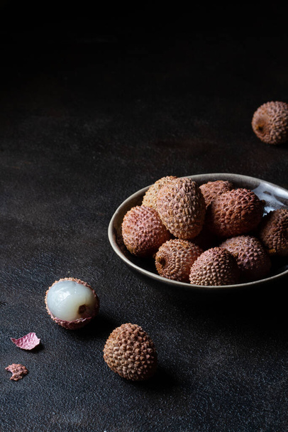 Pink lychees in a ceramic bowl on a dark brown background. Free place. - Foto, afbeelding