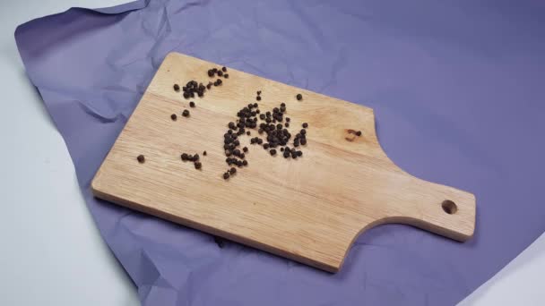 Erwten van zwarte peper gegoten op een houten snijplank, liggend op verfrommeld papier, schenkt de hand van een vrouw kruiden - Video