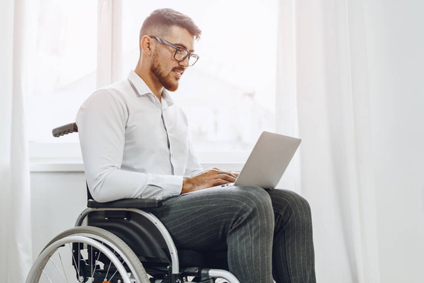 Businessman sitting in wheelchair and using laptop - Foto, afbeelding