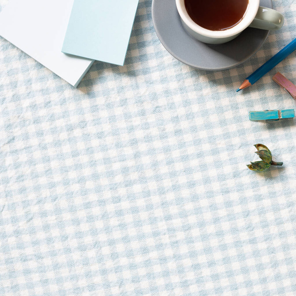 Work and study place. Cup of coffee, notepad, colored pencil, clip on blue check pattern fabric background. flat lay, top view, copy space - Photo, Image