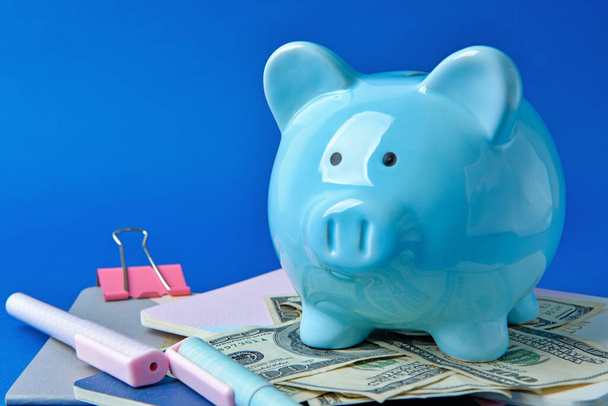 Piggy bank with money and stationery on color background - Foto, afbeelding