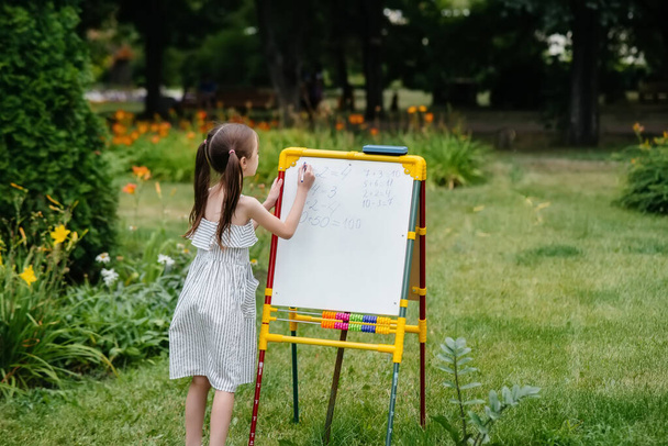 A schoolgirl writes lessons on a blackboard and is engaged in outdoor training. Back to school, learning during the pandemic - Fotografie, Obrázek