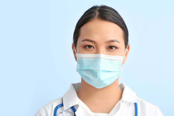 Portrait of female Asian doctor in medical mask on color background - Фото, изображение