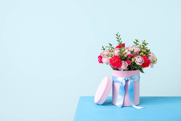 Geschenkdoos met mooie bloemen op tafel tegen een achtergrond van kleur - Foto, afbeelding