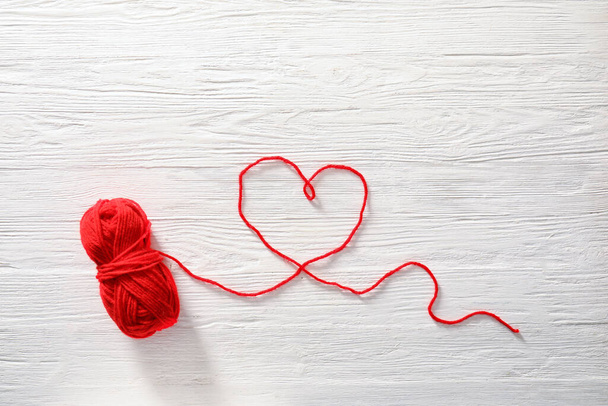 Corazón hecho de hilo de punto rojo sobre fondo de madera blanco - Foto, imagen