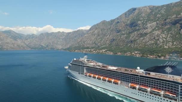 Het cruiseschip vaart langs de baai van Kotor, daarachter liggen prachtige bergen, kiezelstenen zijn zichtbaar in het heldere water, vanuit de lucht gezien - Video