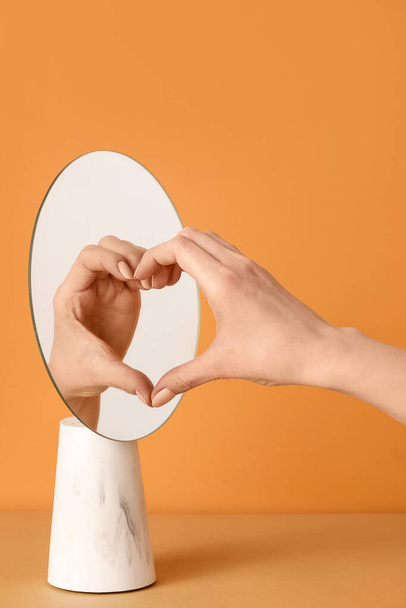 Vrouwelijke hand en haar reflectie in spiegel maken hart tegen kleur achtergrond - Foto, afbeelding
