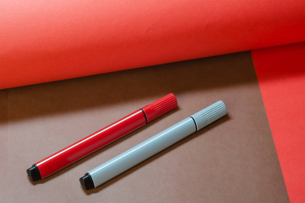 Composição de duas cores minimalista criativa com duas canetas de feltro multicoloridas. As canetas cinzentas e vermelhas da feltro-ponta em um fundo zoneado marrom e vermelho. - Foto, Imagem