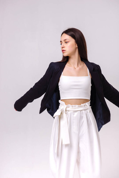 Fashion portrait of a beautiful brunette in white eco pants and a dark jacket on a white background. Eco clothing concept - Photo, Image