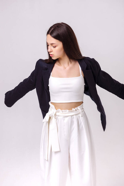 Retrato de moda de una hermosa morena en pantalones ecológicos blancos y una chaqueta oscura sobre un fondo blanco. Concepto de ropa ecológica - Foto, Imagen