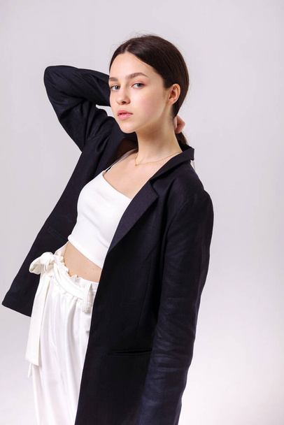 Fashion portrait of a beautiful brunette in white eco pants and a dark jacket on a white background. Eco clothing concept - 写真・画像