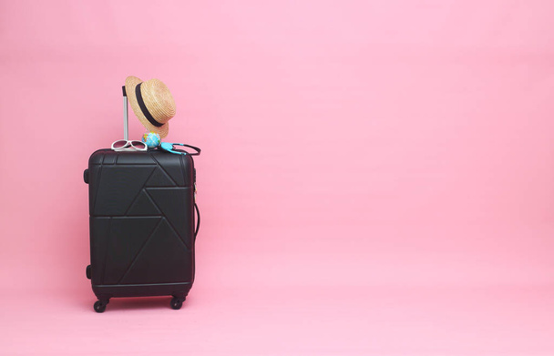 Černý kufr se slunečními brýlemi, klobouk na pastelově růžovém pozadí. cestovní koncept. minimální styl - Fotografie, Obrázek